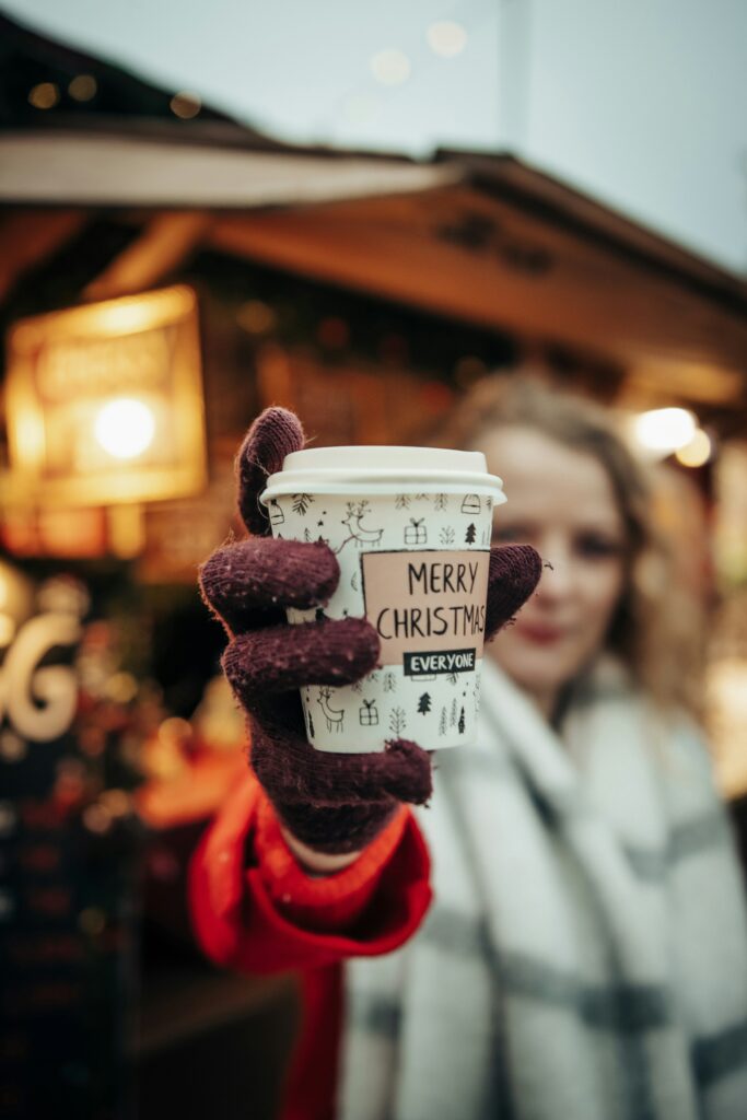 A lady holding a cup of hot cocoa. The cup says "Merry Christmas Everyone"