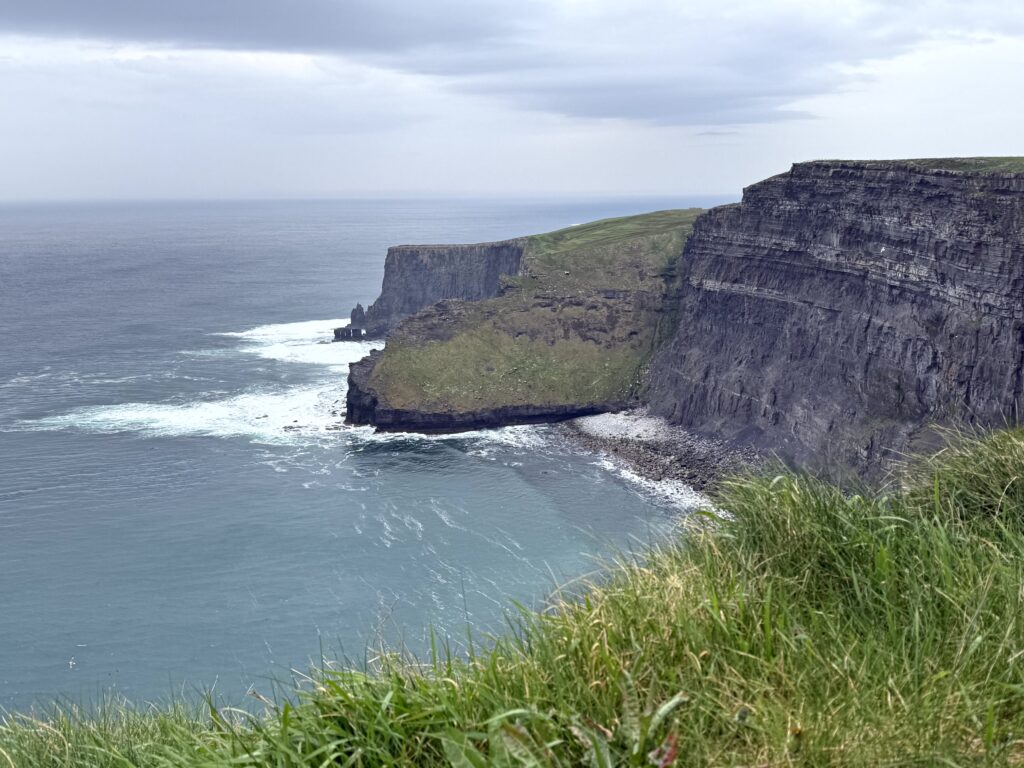 Rolling green hills of the Irish countryside with dramatic coastal cliffs in the background — Ireland landscape photography. They can be seen on a guided Ireland group tour
