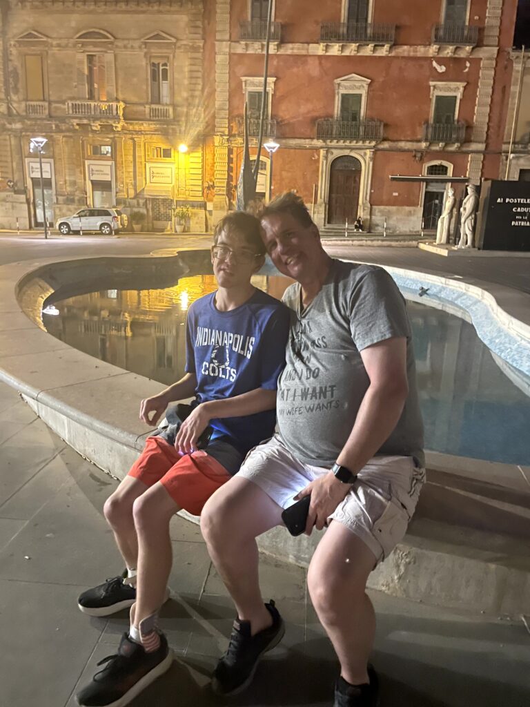 Jim and Aaron sitting by the fountain in a Ragusa square at night.